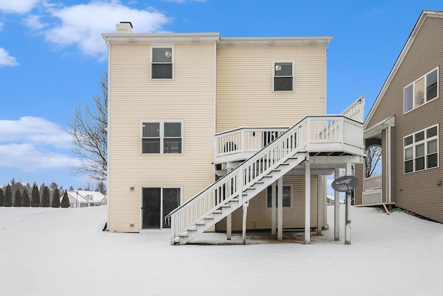 snow covered back of property with a deck and stairs