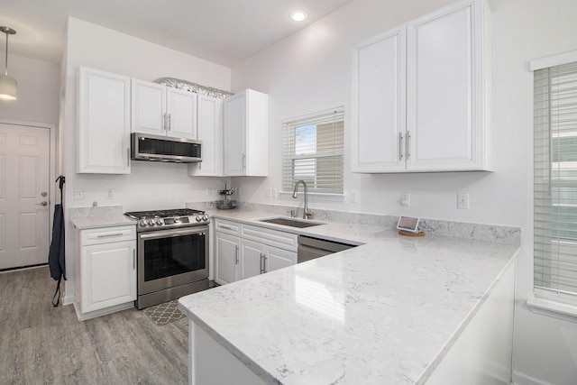 kitchen featuring a sink, white cabinetry, light wood-style floors, appliances with stainless steel finishes, and pendant lighting