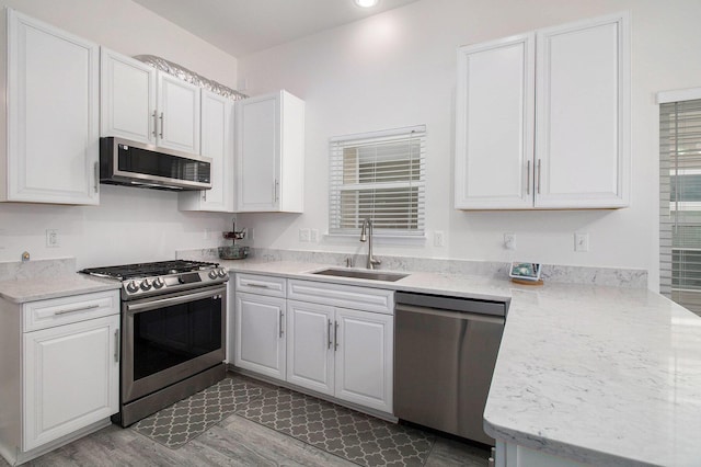 kitchen featuring appliances with stainless steel finishes, white cabinets, a sink, and wood finished floors