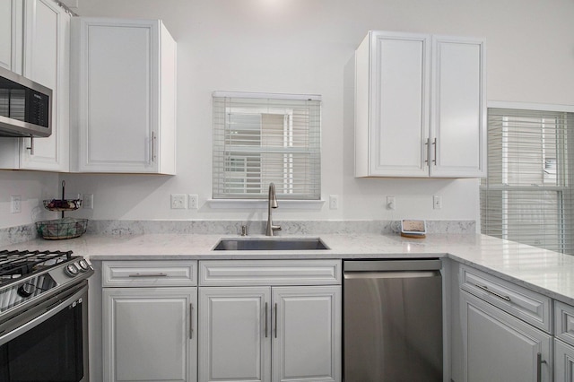 kitchen featuring white cabinetry, appliances with stainless steel finishes, light stone counters, and a sink