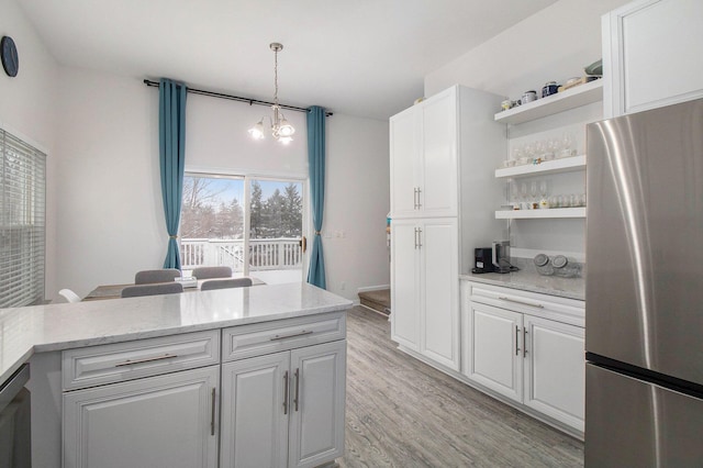 kitchen featuring light stone counters, decorative light fixtures, freestanding refrigerator, and white cabinets