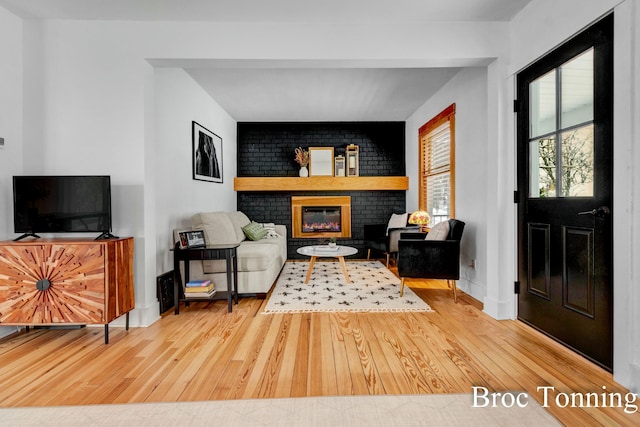 living room featuring light wood-type flooring, a brick fireplace, and baseboards