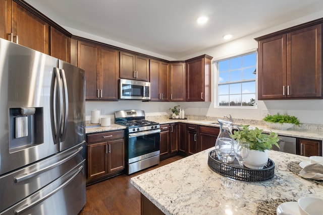 kitchen featuring light stone countertops, dark wood-style floors, stainless steel appliances, and a sink