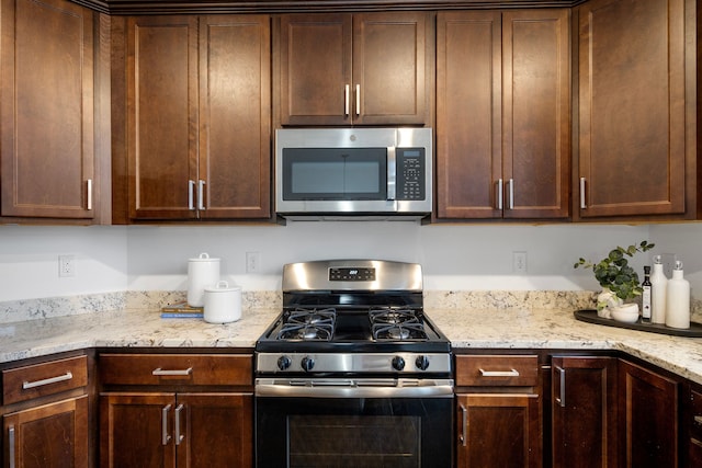 kitchen with stainless steel appliances, light stone counters, and dark brown cabinets