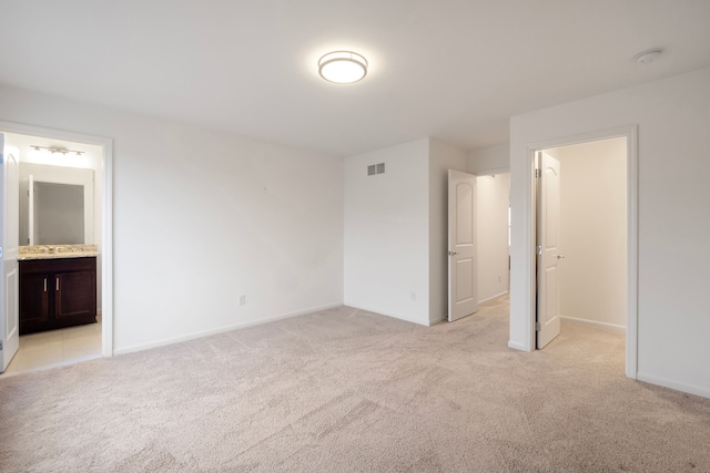 unfurnished bedroom featuring a walk in closet, visible vents, ensuite bathroom, light carpet, and baseboards