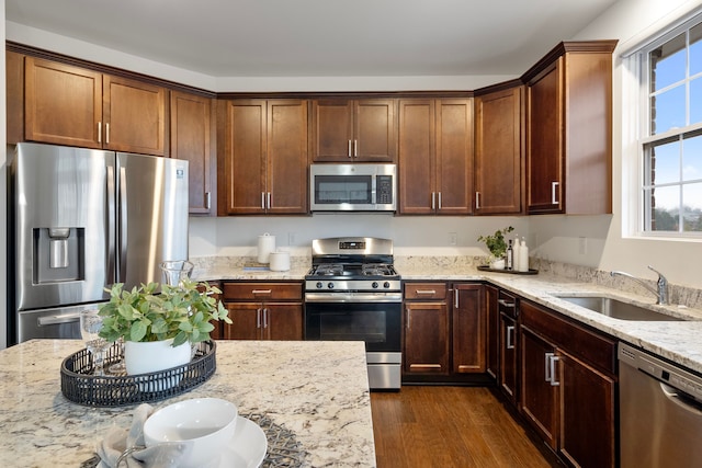 kitchen with stainless steel appliances, light stone countertops, a sink, and dark wood-style floors