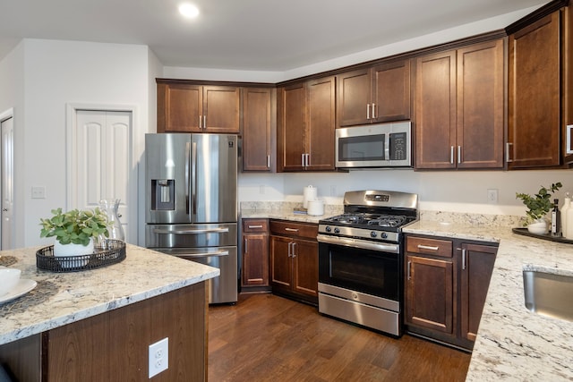 kitchen featuring stainless steel appliances, dark wood-style flooring, dark brown cabinets, and light stone countertops