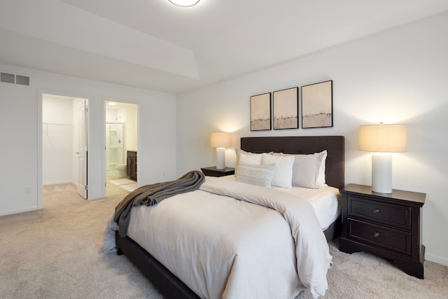 bedroom with a walk in closet, visible vents, light carpet, ensuite bath, and baseboards