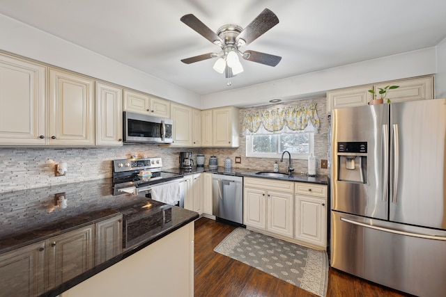 kitchen featuring cream cabinets, stainless steel appliances, a sink, dark stone counters, and dark wood finished floors