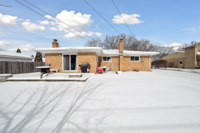 snow covered house with brick siding, a chimney, and fence