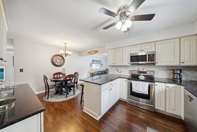 kitchen with stainless steel appliances, a peninsula, decorative backsplash, dark countertops, and dark wood finished floors