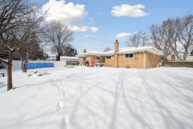 snow covered rear of property with brick siding and a chimney