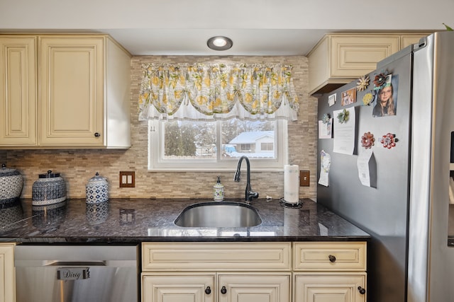 kitchen with dark stone counters, cream cabinetry, a sink, and appliances with stainless steel finishes