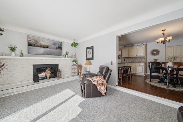 living area featuring a chandelier, dark colored carpet, and a brick fireplace