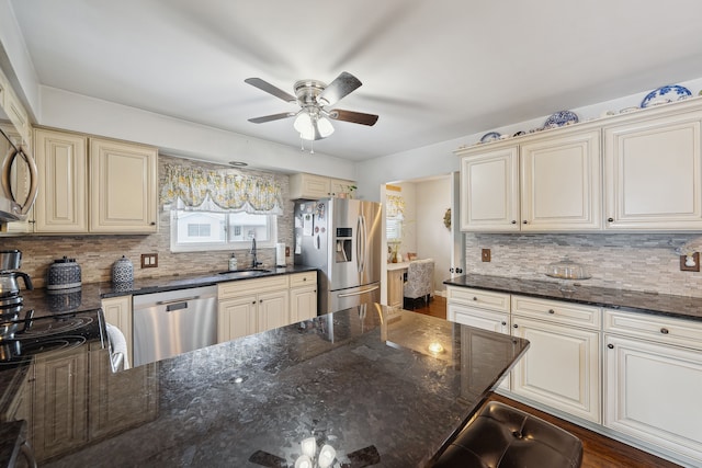 kitchen featuring stainless steel appliances, tasteful backsplash, cream cabinets, a sink, and dark stone counters