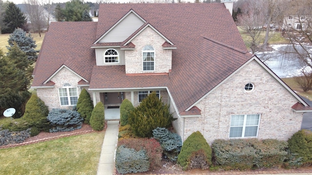 view of front of home with a shingled roof, brick siding, and a chimney