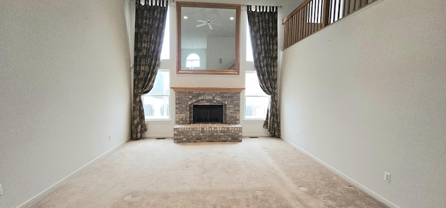 unfurnished living room with light carpet, a brick fireplace, a towering ceiling, and baseboards