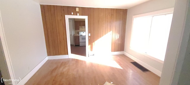 empty room featuring light wood-type flooring, wood walls, baseboards, and visible vents