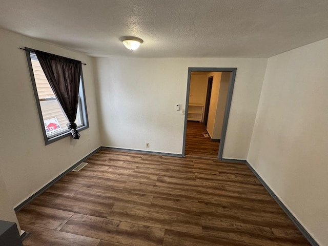 empty room featuring baseboards, a textured ceiling, visible vents, and dark wood-type flooring