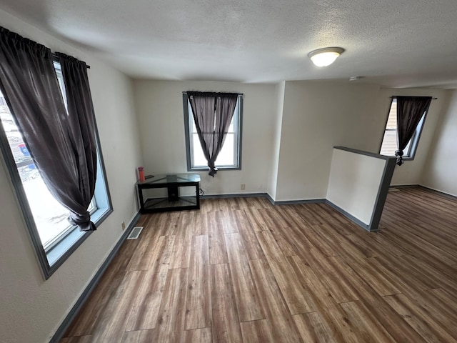 spare room featuring a textured ceiling, dark wood-type flooring, visible vents, and baseboards