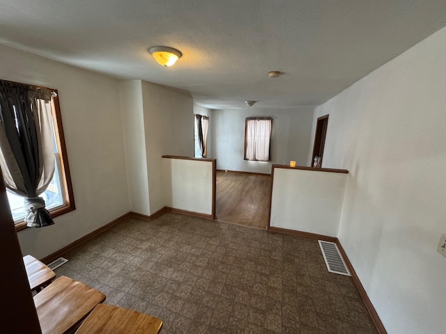 empty room with visible vents, a textured ceiling, baseboards, and tile patterned floors