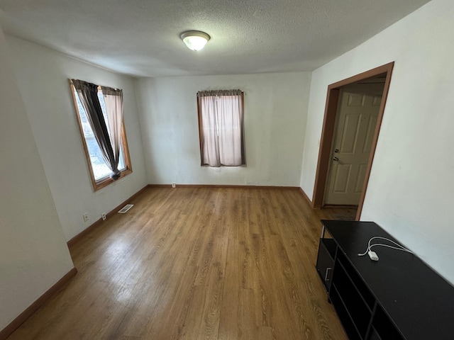 unfurnished room featuring light wood-type flooring, baseboards, visible vents, and a textured ceiling