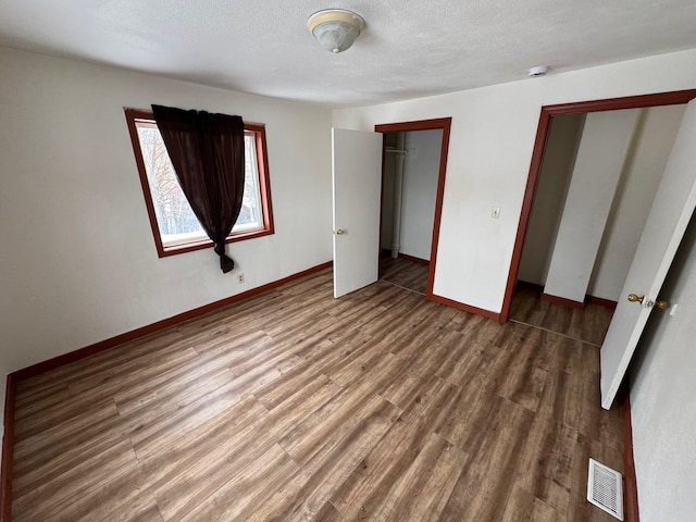 unfurnished bedroom with baseboards, a textured ceiling, visible vents, and dark wood-style flooring