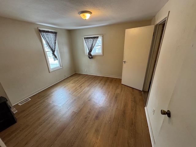 unfurnished bedroom with a textured ceiling, wood finished floors, visible vents, and baseboards