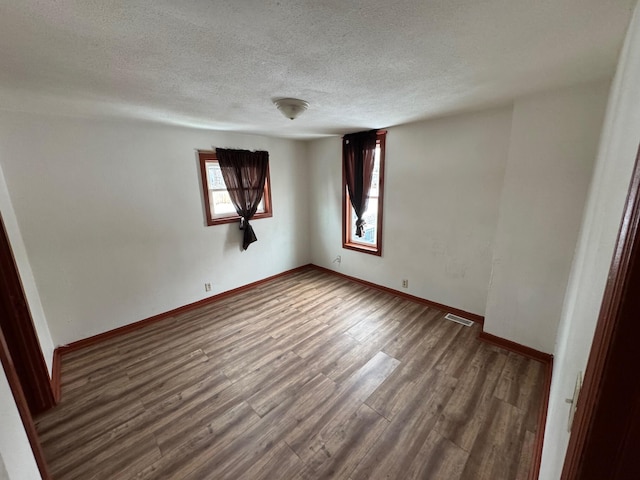 spare room featuring dark wood-style floors, visible vents, a textured ceiling, and baseboards