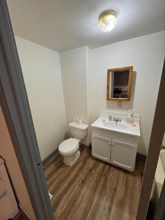 half bathroom with toilet, a textured ceiling, vanity, wood finished floors, and baseboards