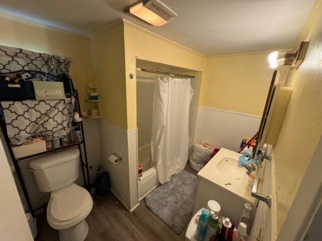 full bathroom with toilet, wood finished floors, vanity, ornamental molding, and shower / bath combination with curtain