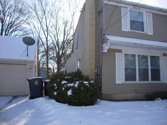 view of snowy exterior with a garage and a chimney