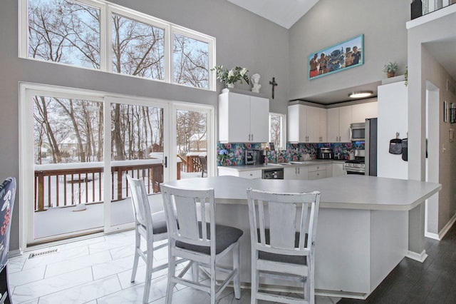 2839 Davista Dr, Highland, MI 48356 - kitchen with stainless steel appliances, high vaulted ceiling, light countertops, white cabinets, and baseboards