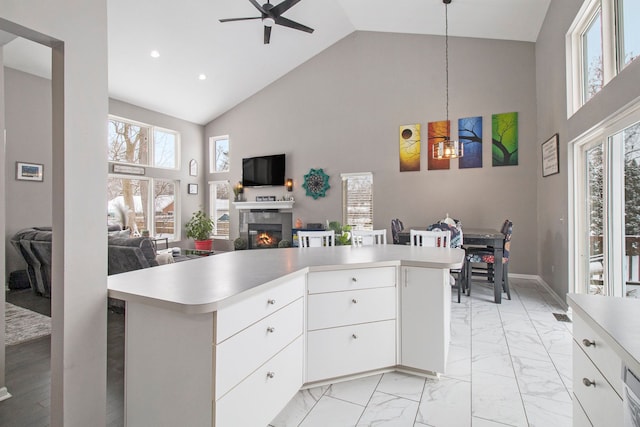 2839 Davista Dr, Highland, MI 48356 - kitchen featuring open floor plan, a ceiling fan, high vaulted ceiling, light countertops, and a glass covered fireplace