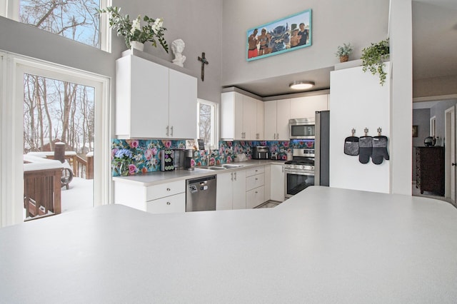 2839 Davista Dr, Highland, MI 48356 - kitchen featuring appliances with stainless steel finishes, decorative backsplash, healthy amount of natural light, white cabinetry, and a towering ceiling