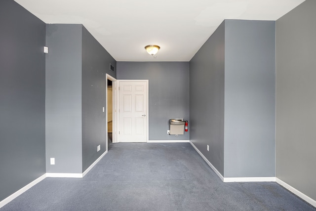 empty room with dark colored carpet, visible vents, and baseboards