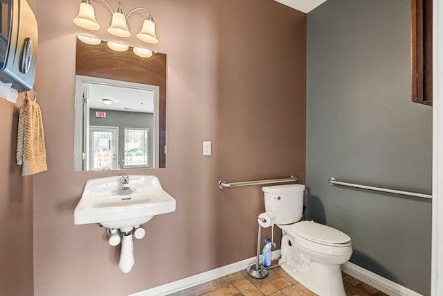 half bathroom featuring baseboards, toilet, an inviting chandelier, stone finish flooring, and a sink