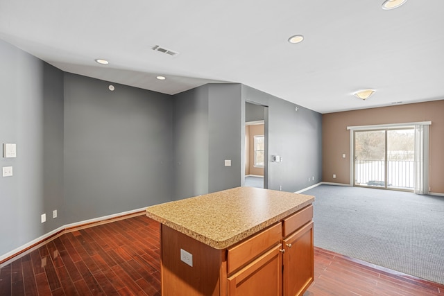 kitchen featuring visible vents, brown cabinets, open floor plan, a center island, and light countertops