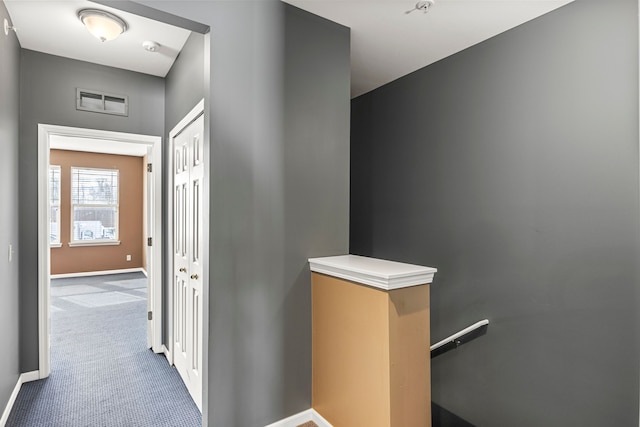 hallway featuring carpet, baseboards, visible vents, and an upstairs landing