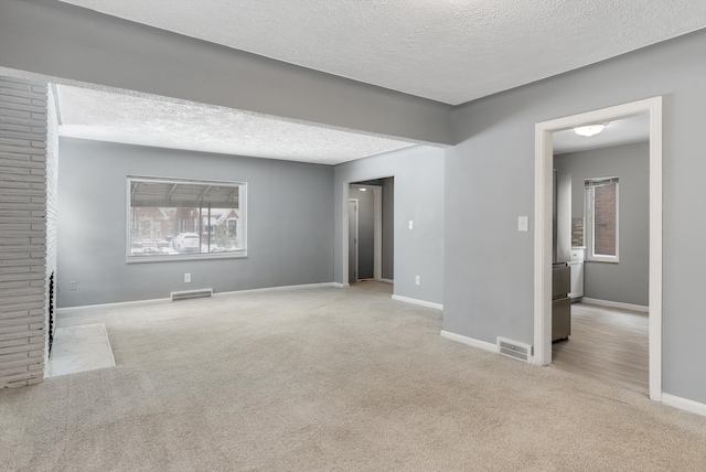 unfurnished room featuring light colored carpet, visible vents, a textured ceiling, and baseboards