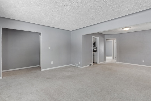 unfurnished room with baseboards, a textured ceiling, visible vents, and light colored carpet