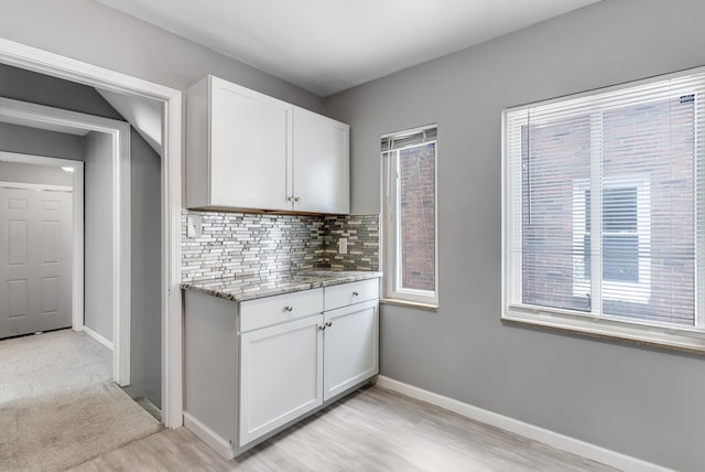 kitchen with light stone counters, light wood-style flooring, backsplash, white cabinetry, and baseboards