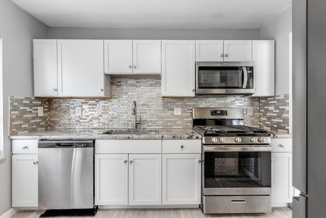 kitchen featuring light stone counters, appliances with stainless steel finishes, white cabinets, and a sink