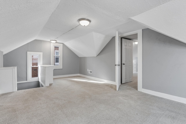 additional living space featuring a textured ceiling, baseboards, lofted ceiling, and light colored carpet