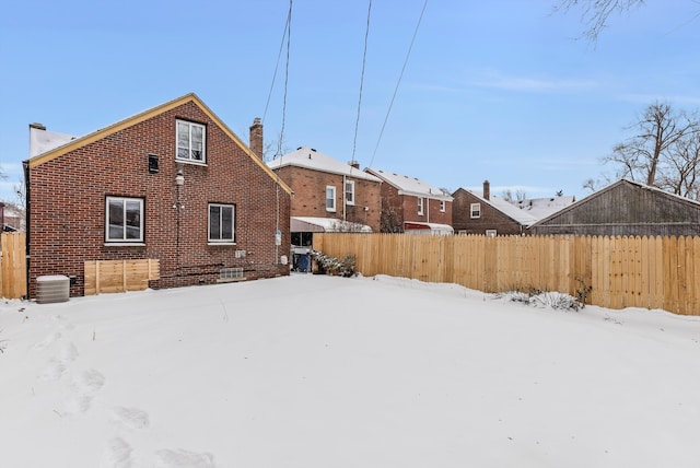 snow covered property featuring central air condition unit, a chimney, fence, and brick siding