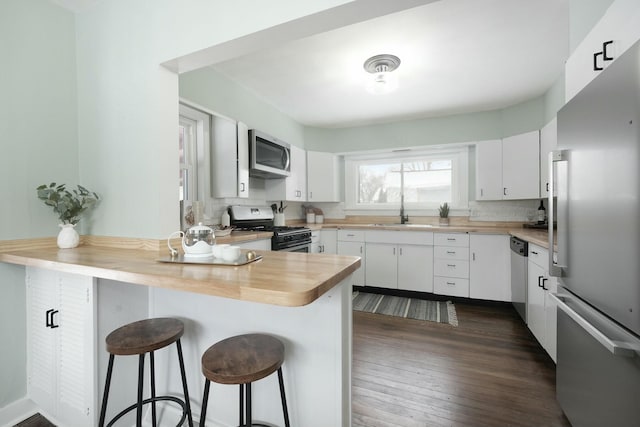 kitchen with stainless steel appliances, white cabinets, a peninsula, and a kitchen bar