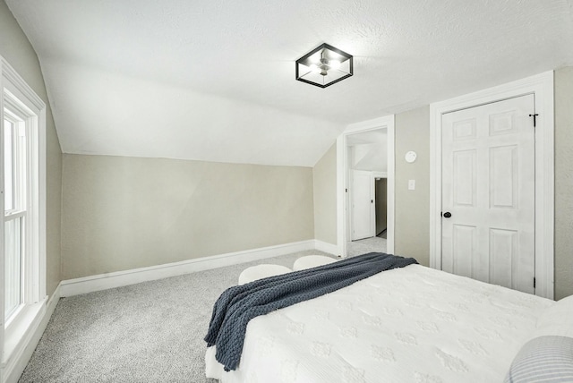 bedroom with carpet floors, vaulted ceiling, a textured ceiling, and baseboards