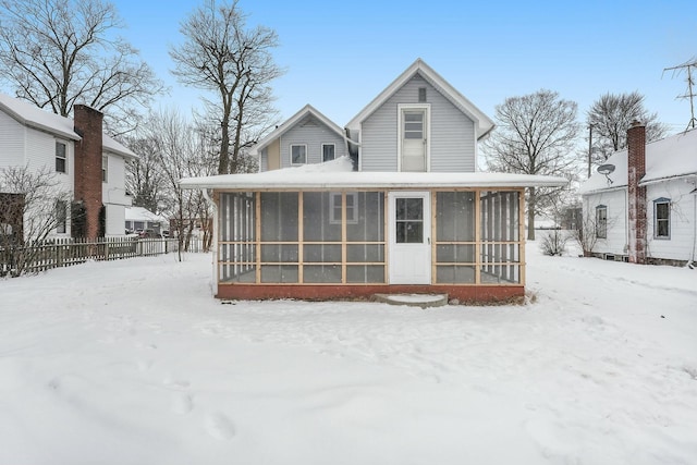 snow covered back of property with a sunroom and fence