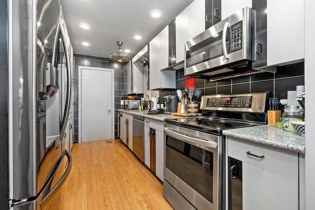 kitchen with stainless steel appliances, recessed lighting, tasteful backsplash, white cabinets, and light wood-type flooring