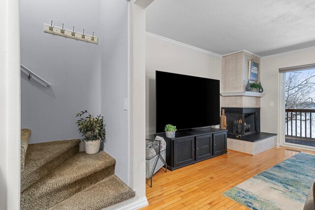 living room featuring stairs, ornamental molding, a tiled fireplace, and wood finished floors